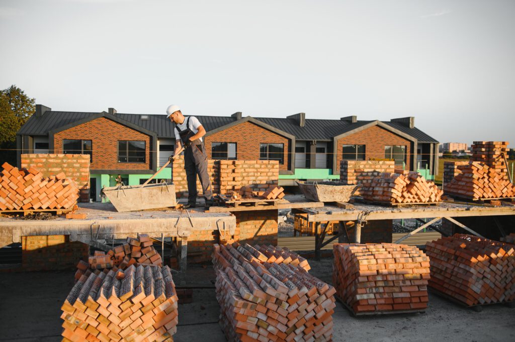 Bouwvakker met helm en werkuitrusting aan het werk op een woningbouwproject met bakstenen en gereedschap op de bouwplaats.