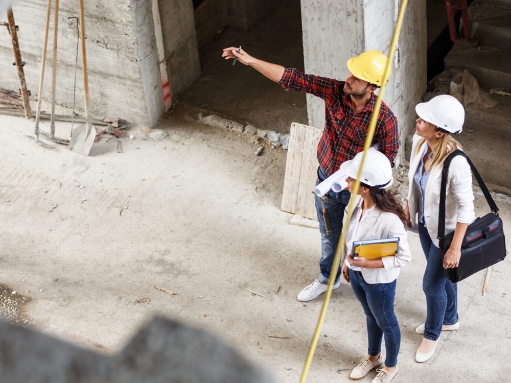Bouwspecialisten met helmen bespreken een project op een bouwplaats, waarbij de aannemer aanwijzingen geeft aan het team.