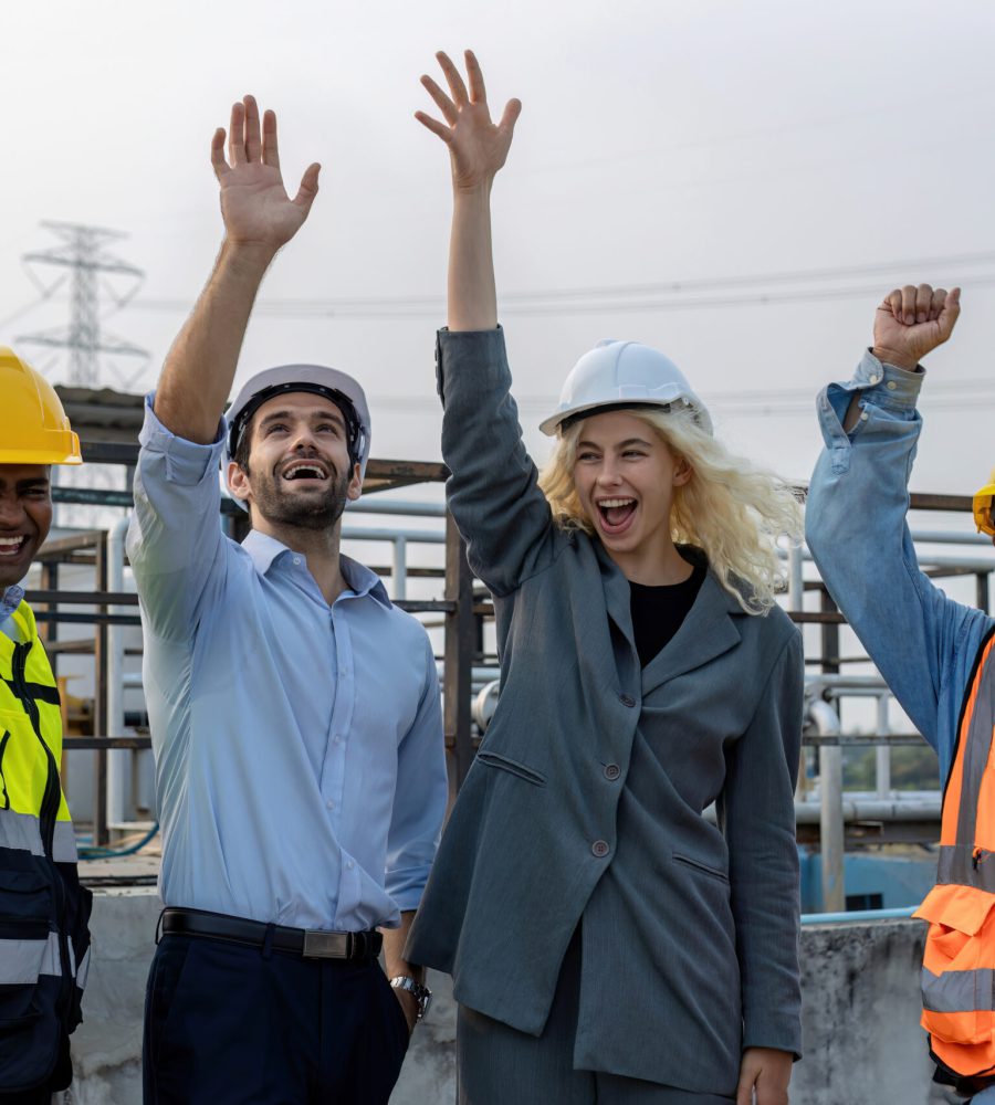 Een enthousiast team van aannemers en bouwspecialisten viert een succesvol bouwproject met opgeheven handen op een bouwplaats.